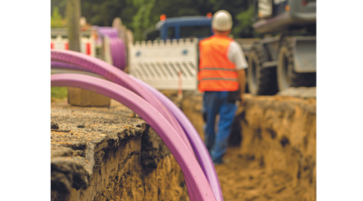 close up of purple ducting in trench, workman in background