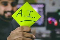 Man holding a post-it note to the foreground with the letters A.I.