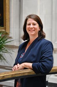 Angela Jones, a white woman in her late 40s, with shoulder-length brown hair, brown eyes, wearing a dark jacket and looking at the camera, leaning on a balustrade